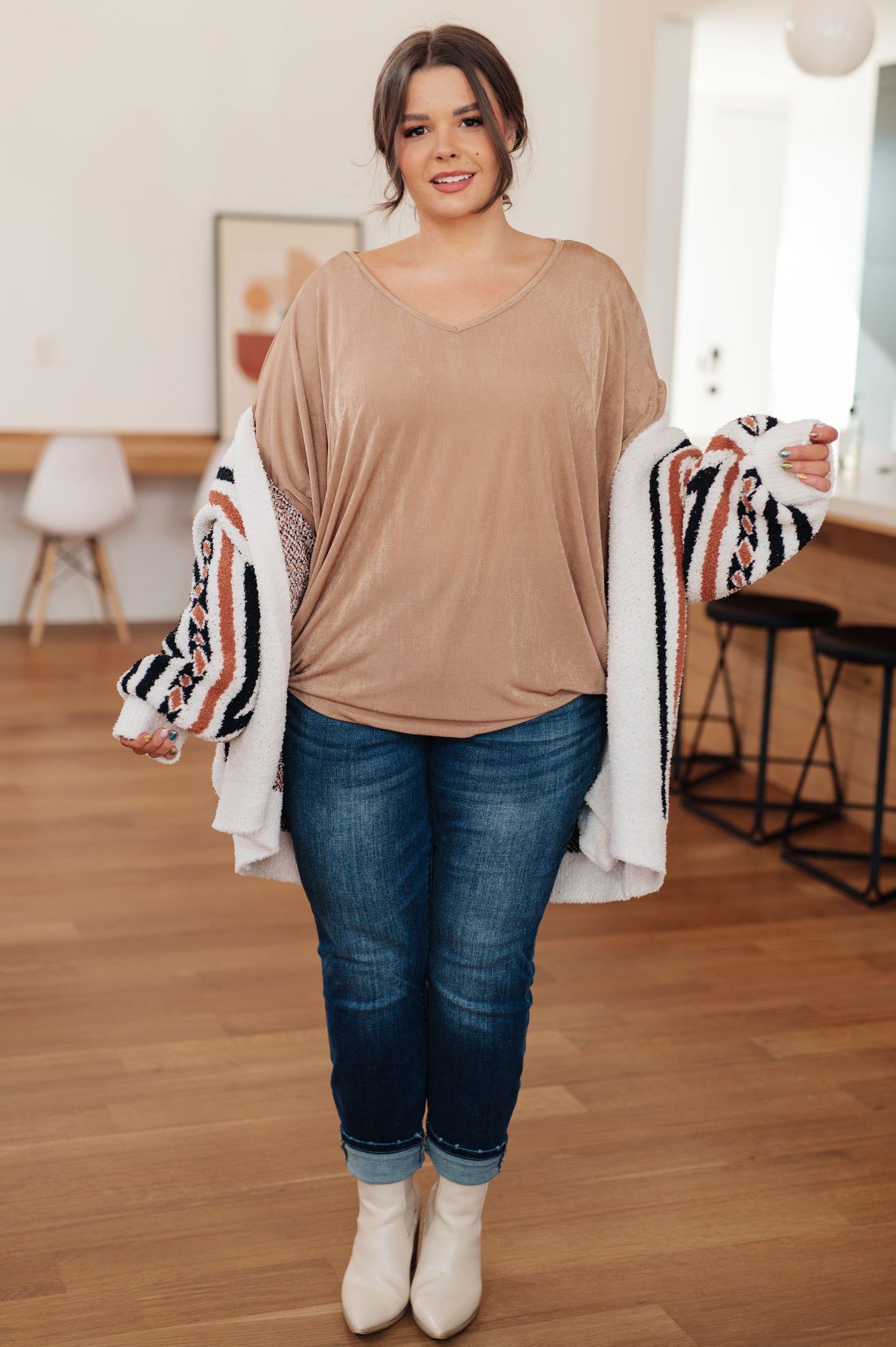 Woman wearing a beige top and blue jeans indoors.