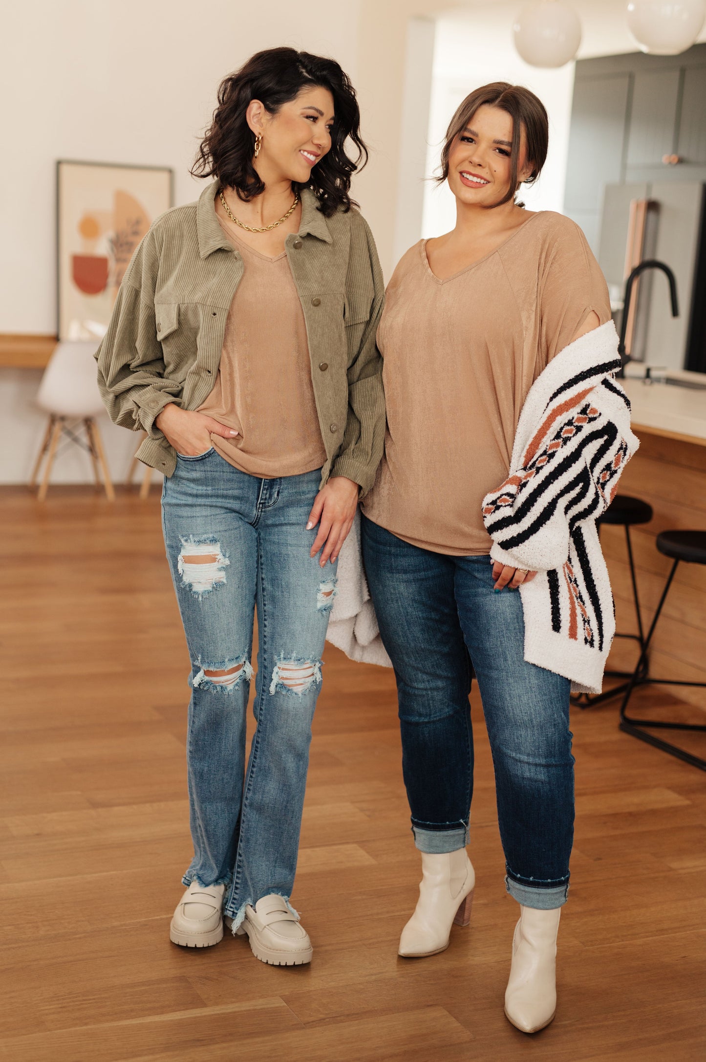 Two women standing indoors wearing casual outfits with jeans and jackets.