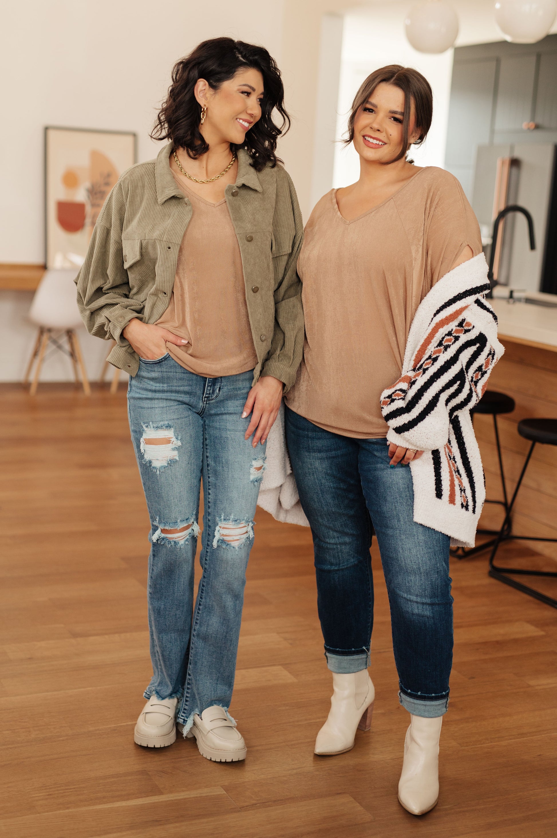 Two women standing indoors wearing casual outfits with jeans and jackets.