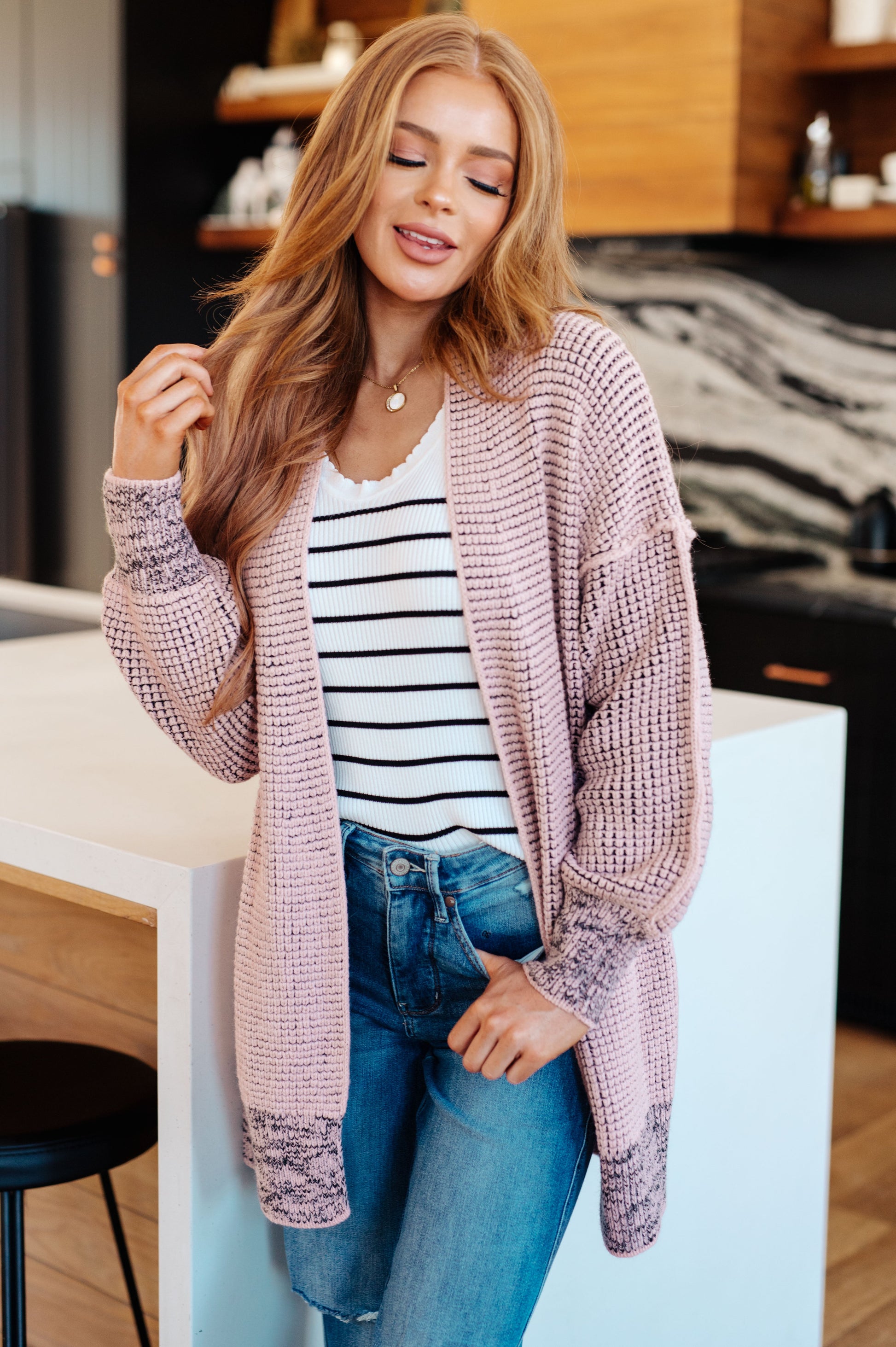 Woman wearing a pink cardigan, striped shirt, and jeans in a kitchen setting
