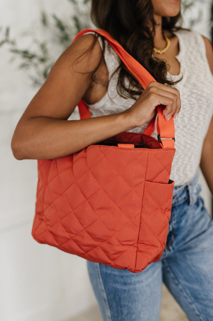 Person holding a red quilted bag with a blurred background