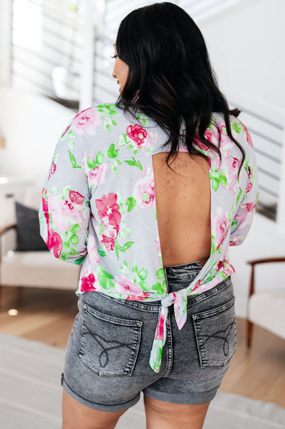 Woman wearing a floral blouse with open back and denim shorts in an indoor setting.