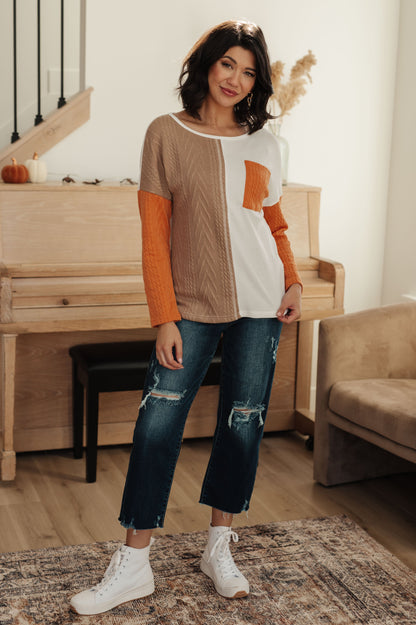 Woman wearing a color-blocked sweater and jeans standing in a room with a piano and sofa.