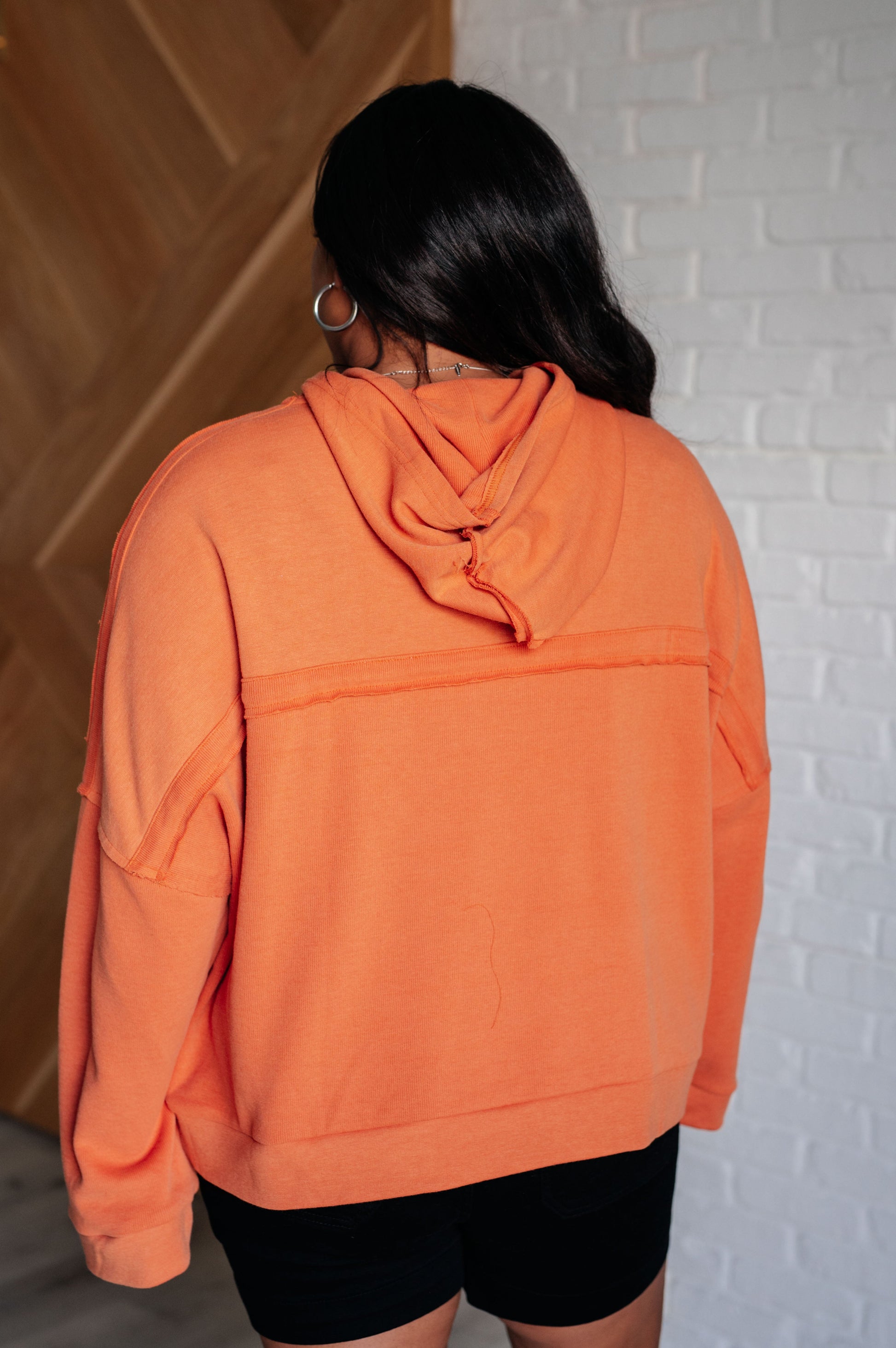 Person wearing an orange hoodie with a white brick wall background