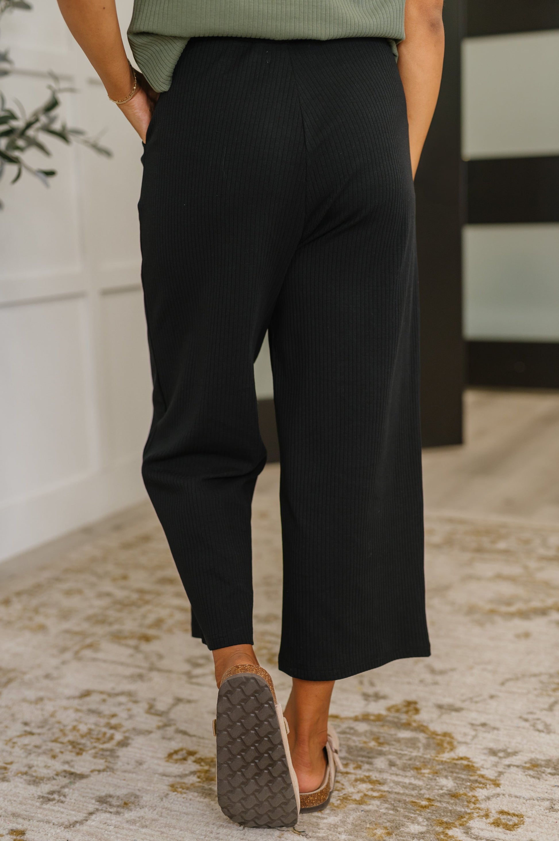 Person wearing black pants and brown shoes on a patterned rug.