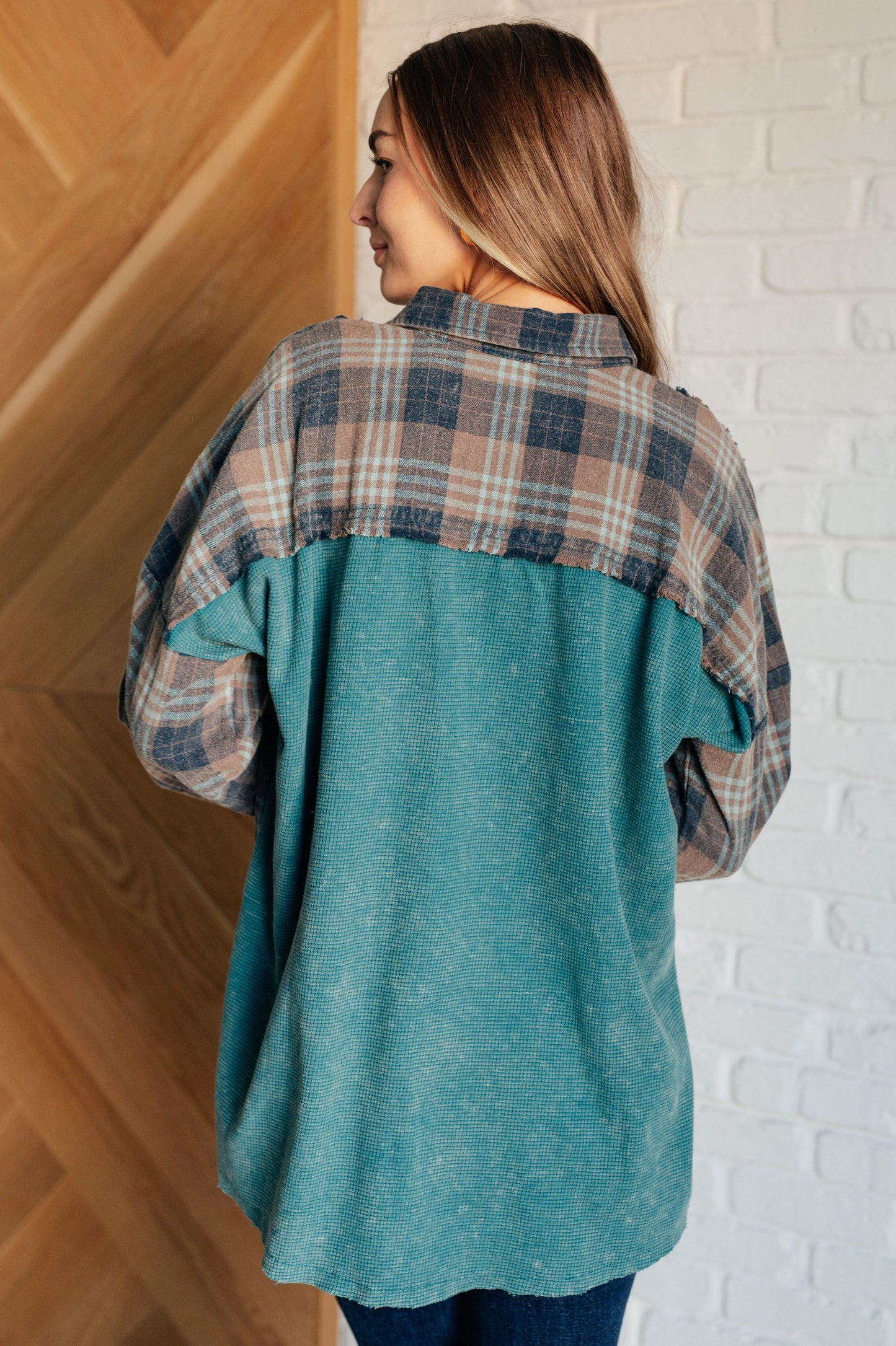 Woman wearing a teal and plaid shirt against a white brick wall.