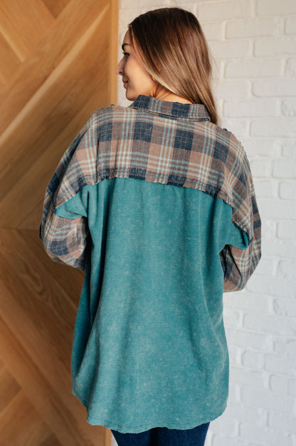 Woman wearing a teal and plaid shirt against a white brick wall.