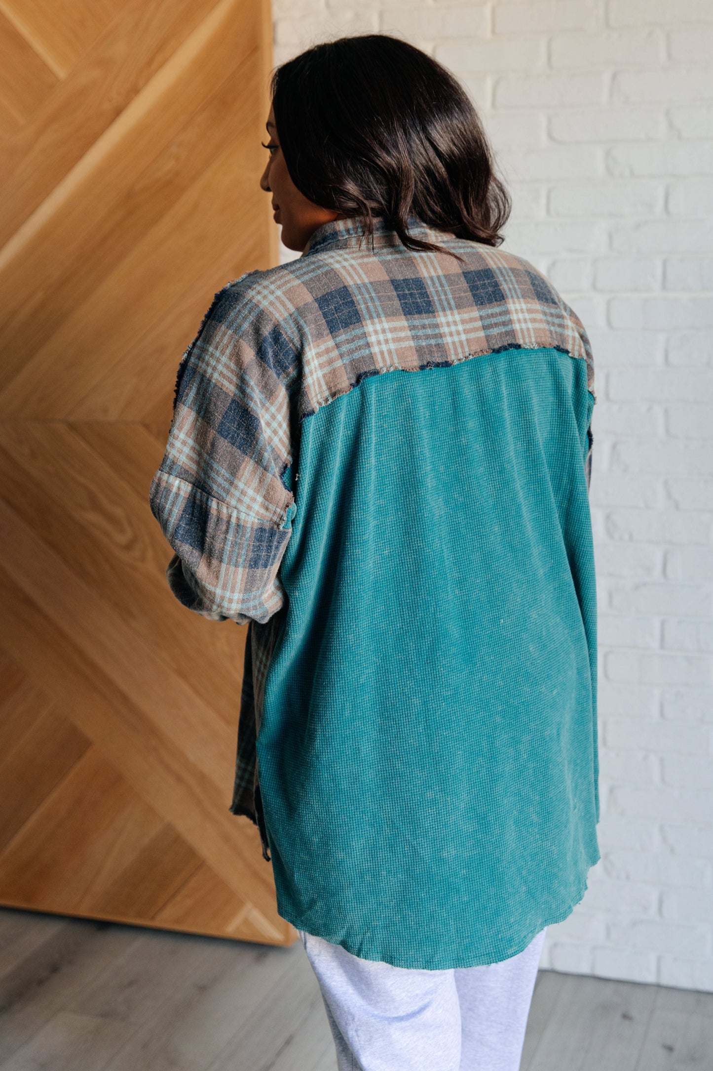 Person wearing a teal and plaid shirt against a wooden wall.