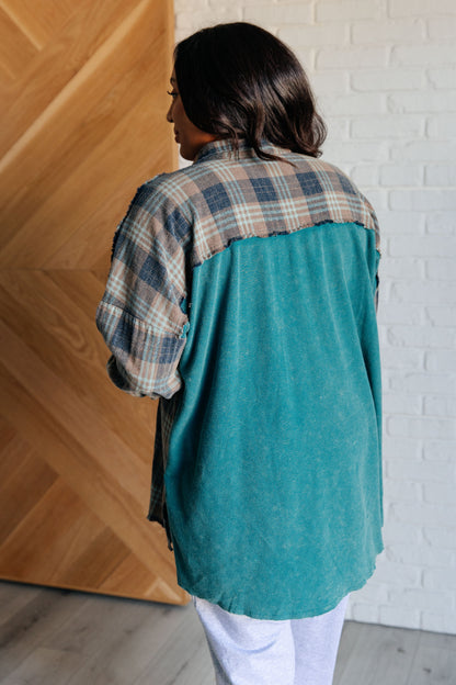 Person wearing a teal and plaid shirt against a wooden wall.