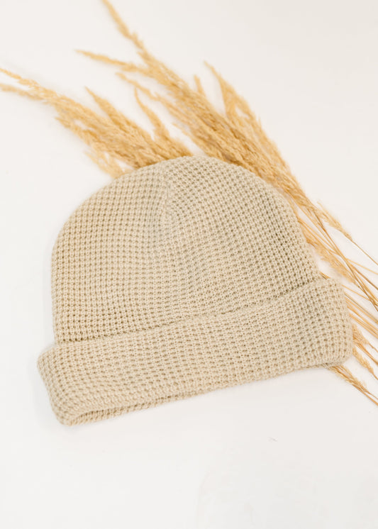 Beige knit beanie on a white background with dried wheat stalks.