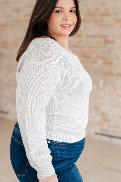 Woman wearing a white sweater and blue jeans against a brick wall.