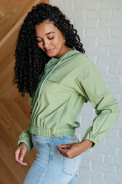 Woman wearing a light green jacket against a white brick wall.