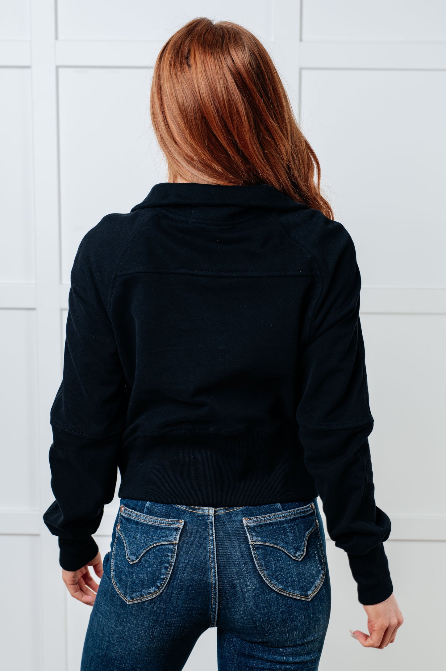 Person wearing a black jacket and blue jeans against a white tiled wall