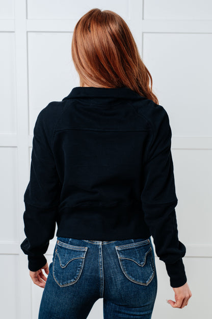 Person wearing a black jacket and blue jeans against a white tiled wall
