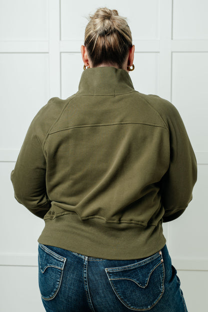 Person wearing an olive green jacket and blue jeans against a white tiled wall.