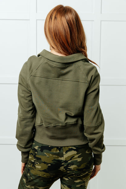 Person wearing a green jacket and camouflage pants against a white tiled wall.