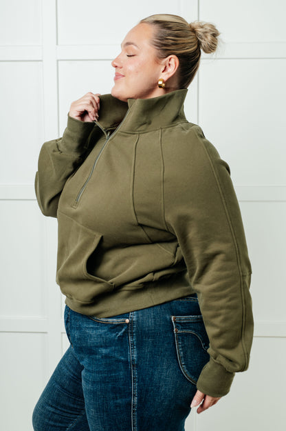 Person wearing an olive green jacket and blue jeans against a white tiled wall.