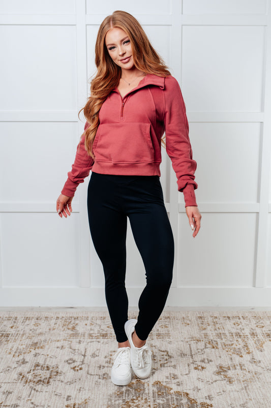 Woman wearing a pink pullover and black leggings against a white wall.