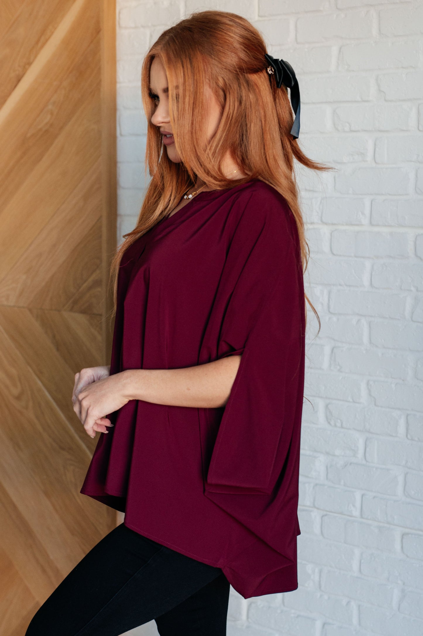 Woman wearing a burgundy top against a white brick wall.