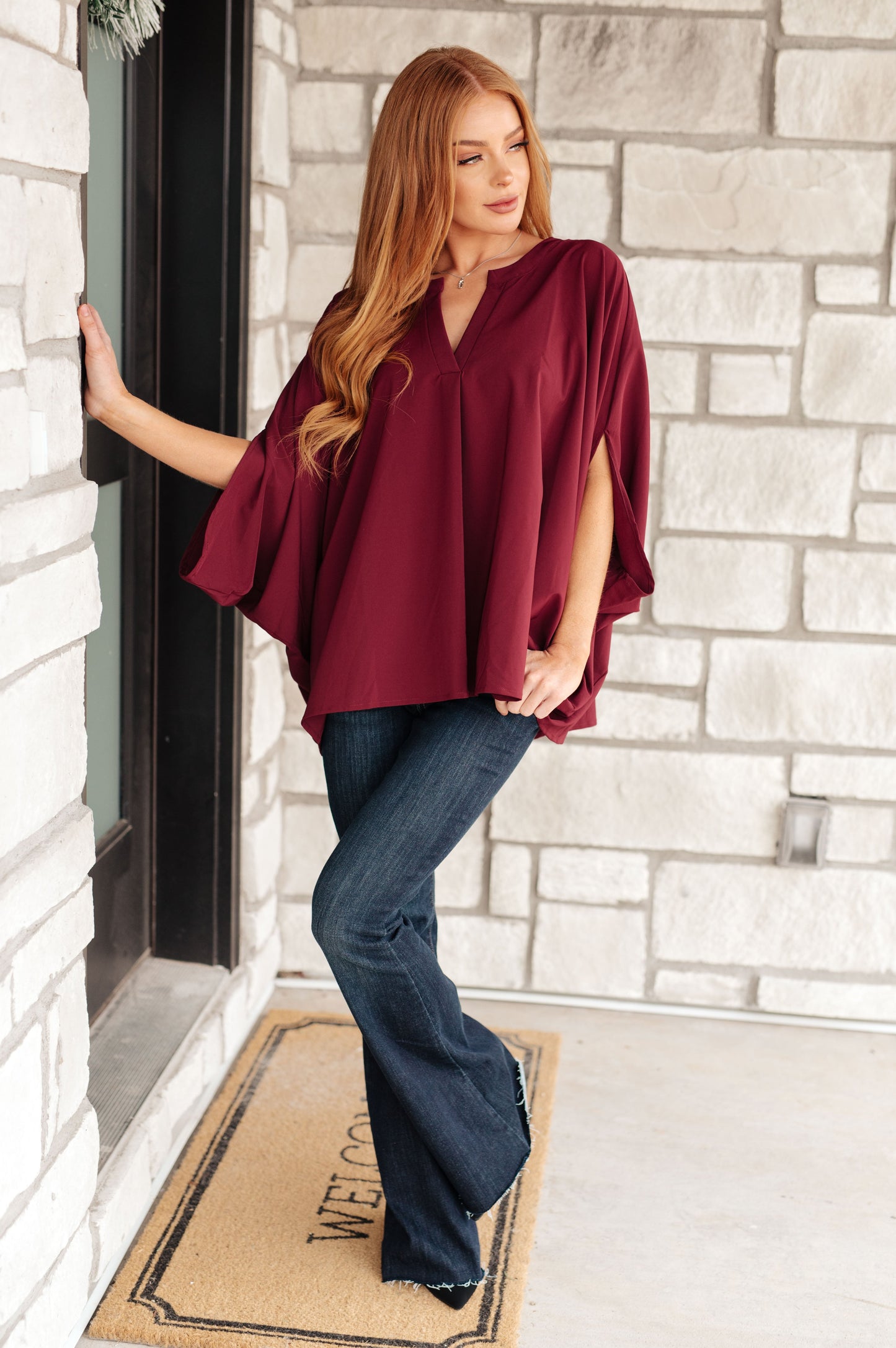 Woman wearing a burgundy top and blue jeans standing in front of a stone wall.