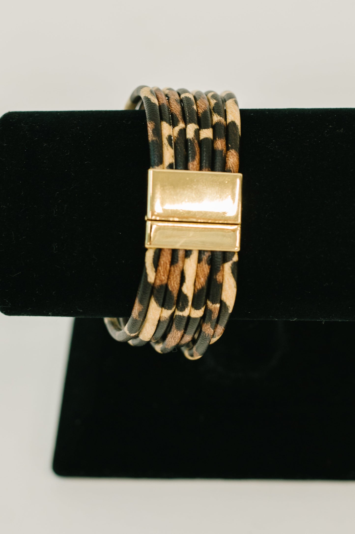 Bracelet with gold clasp on a black stand against a white background