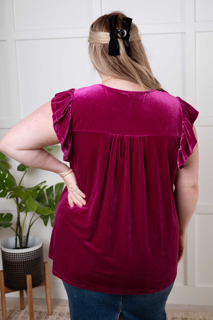 Person wearing a burgundy top with ruffled sleeves in a room with a plant and tiled wall.