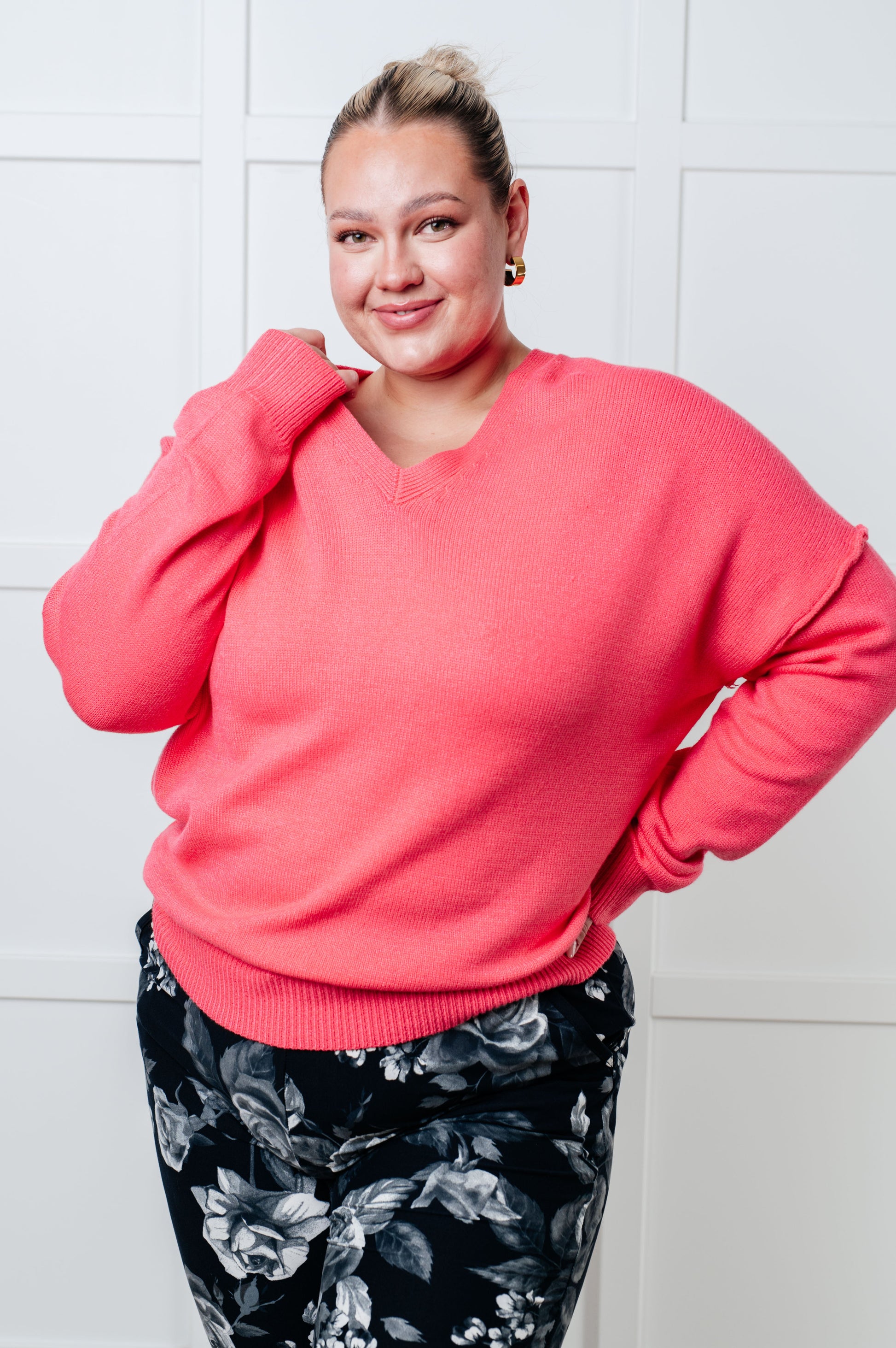Woman wearing a pink sweater and floral pants against a white tiled wall