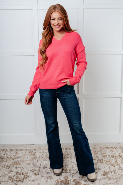 Woman wearing a pink sweater and blue jeans standing against a white wall.