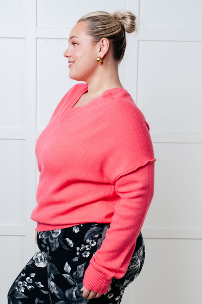 Woman wearing a pink sweater and floral pants against a white tiled wall.