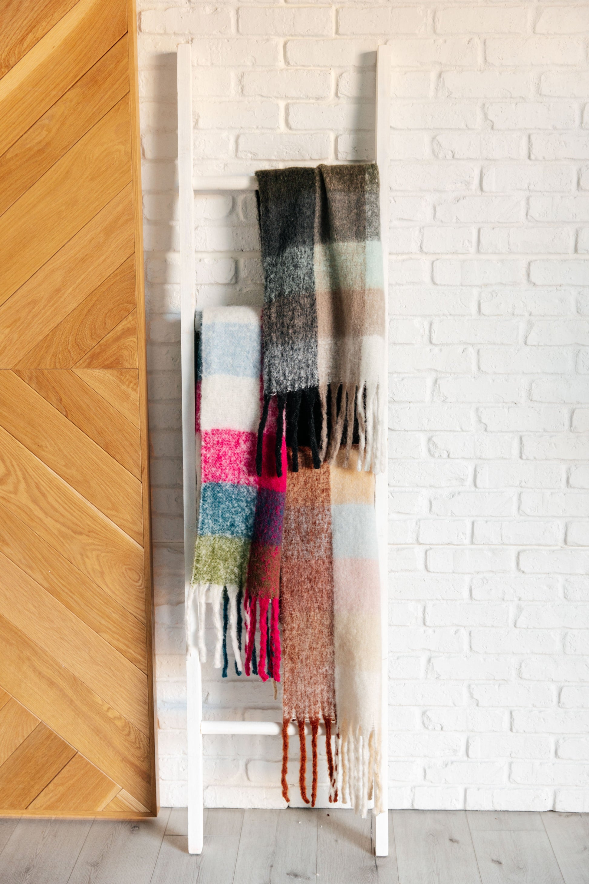 Colorful scarf draped over a white rack against a white brick wall.