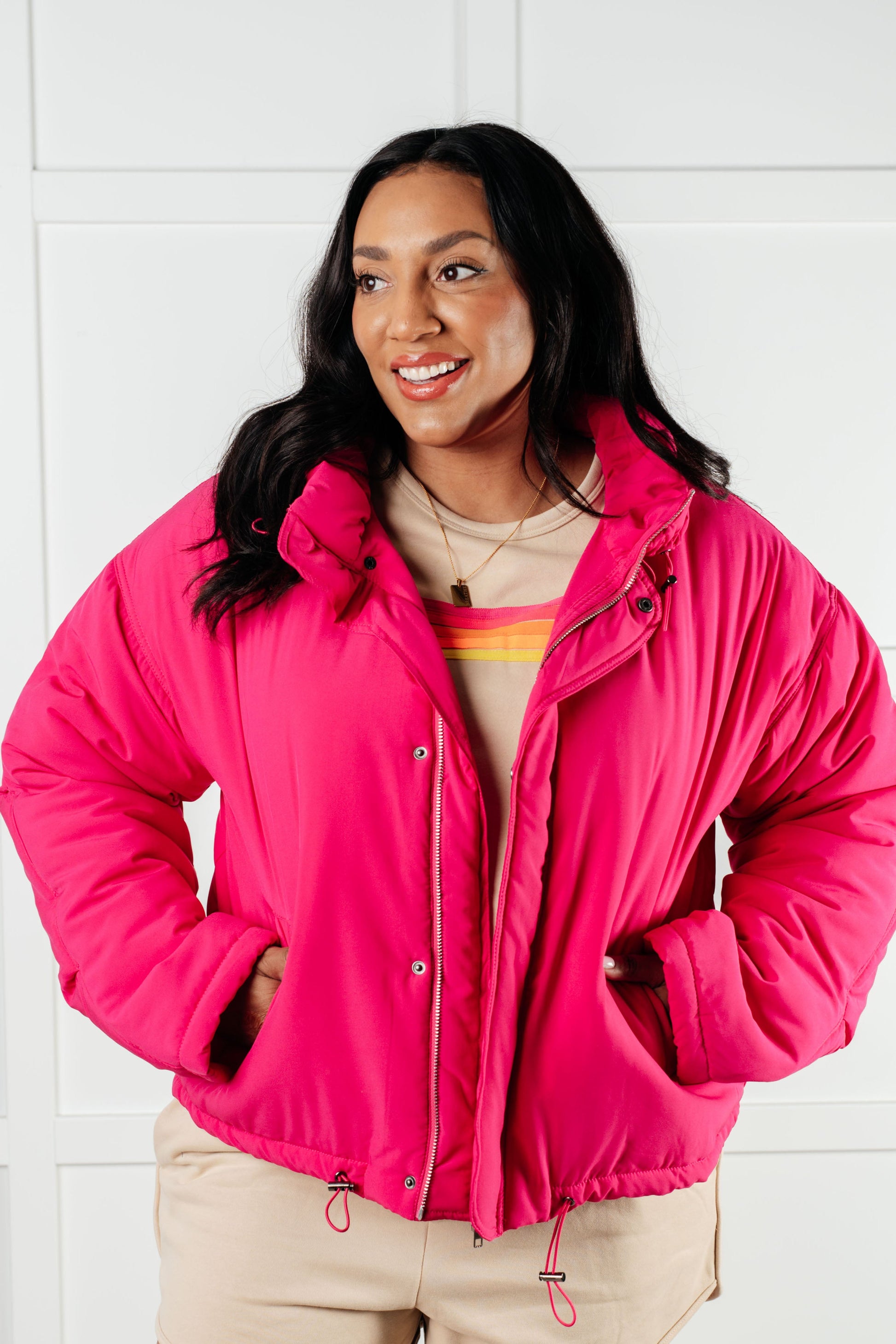 Woman wearing a bright pink jacket against a white tiled wall