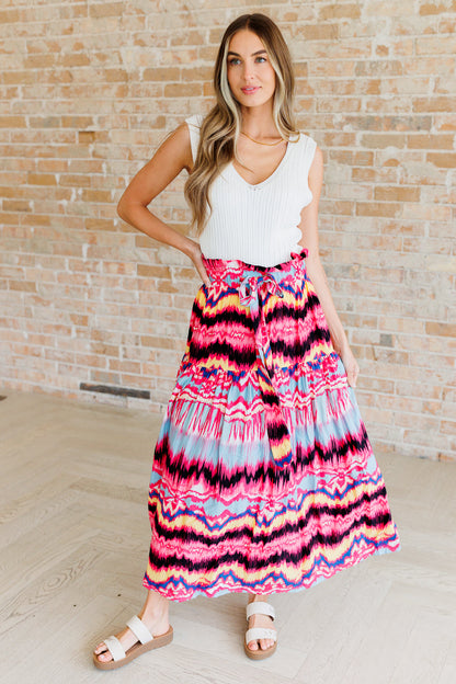 Woman wearing a colorful tie-dye skirt with a white top against a brick wall.
