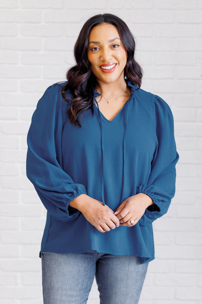 Woman wearing a blue blouse against a white brick wall