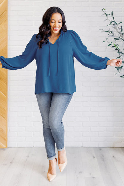 Woman wearing a blue blouse and jeans standing in a room with a white wall and wooden door.
