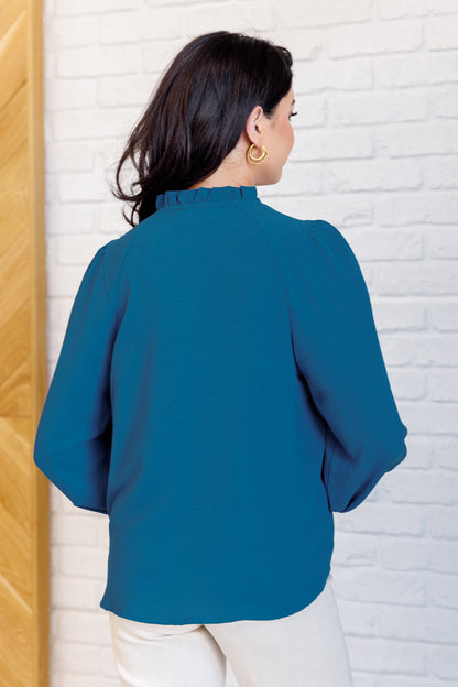 Woman wearing a blue blouse against a white brick wall.