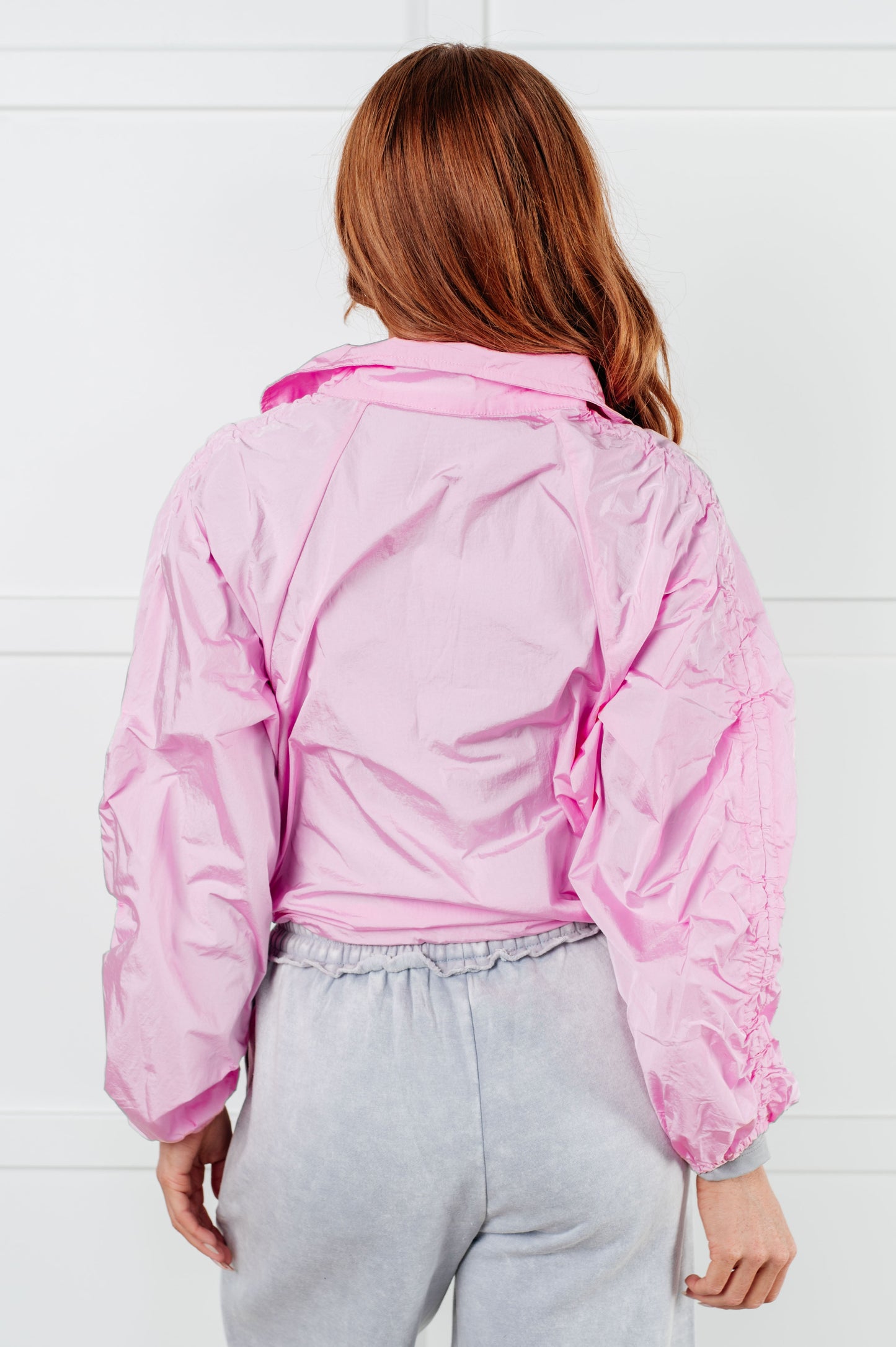 Person wearing a pink jacket against a white tiled wall