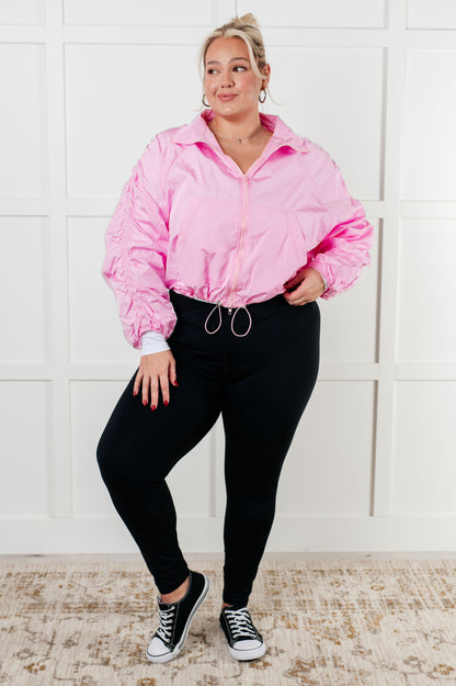 Person wearing a pink jacket and black pants standing against a white tiled wall.
