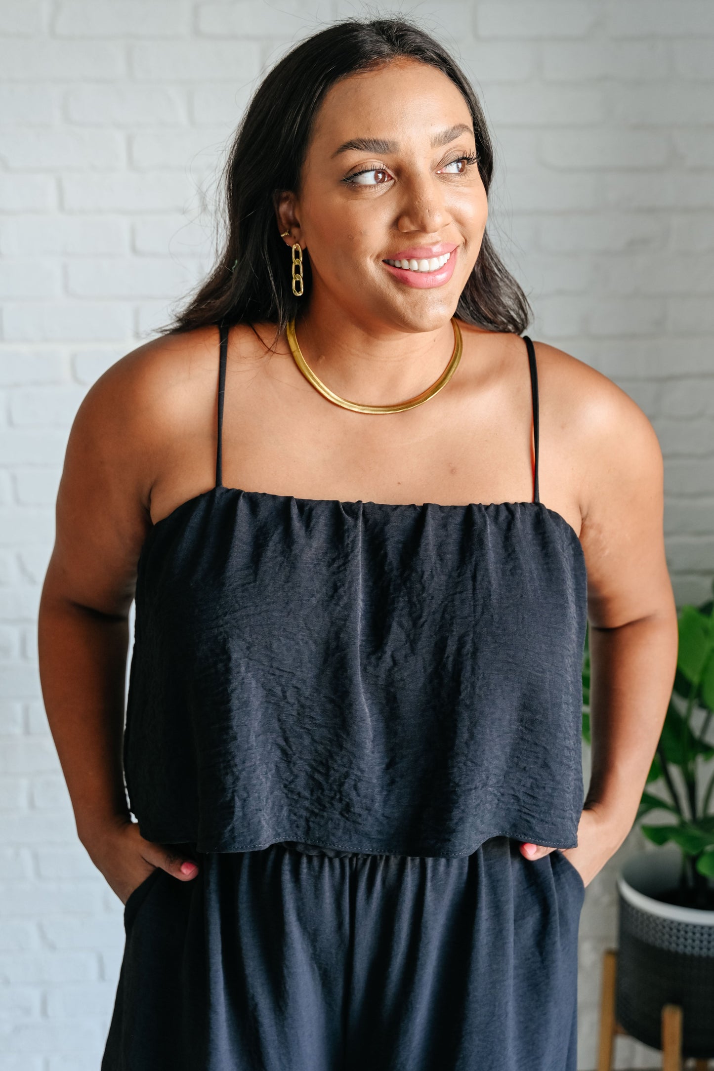 Woman wearing a black top and blue pants against a gray brick wall.