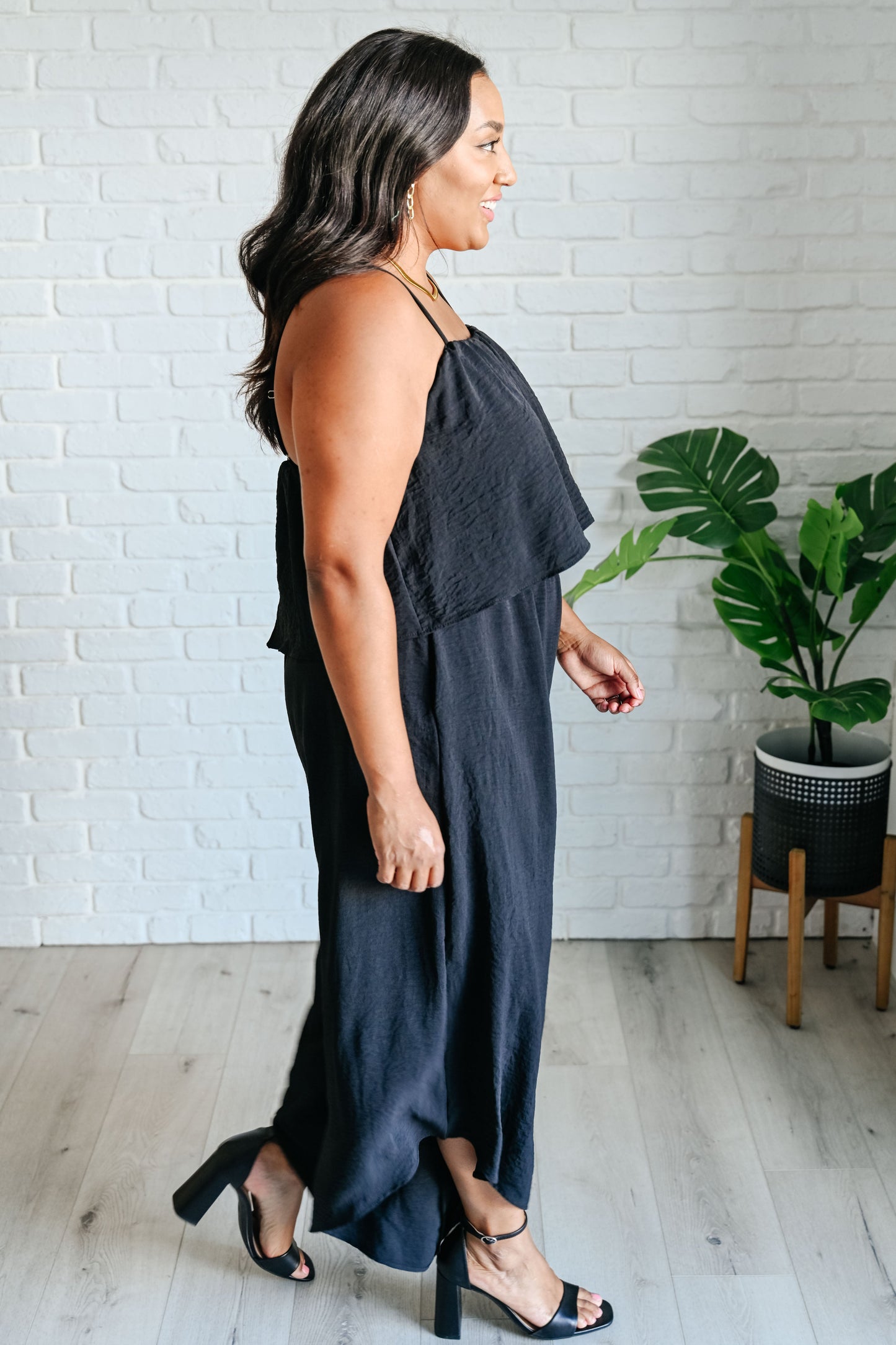 Woman wearing a dark blue dress standing in a room with a white brick wall and a plant.