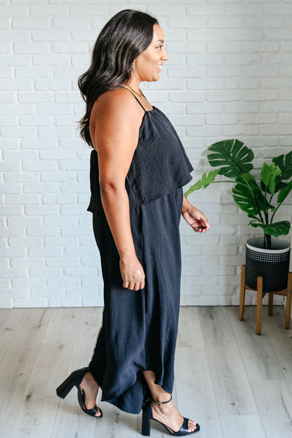 Woman wearing a dark blue dress standing in a room with a white brick wall and a plant.