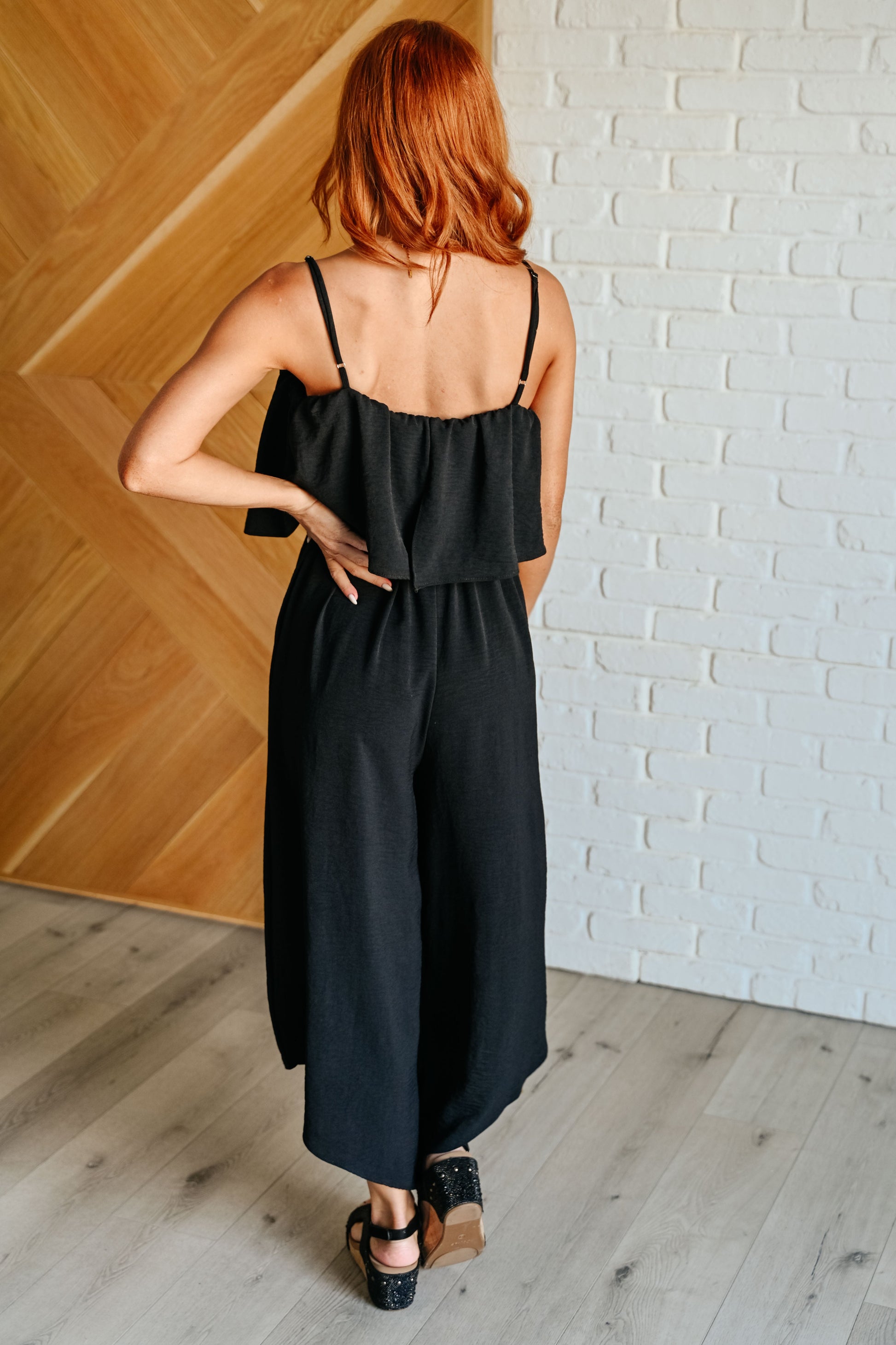 Woman wearing a black dress standing against a white brick wall.