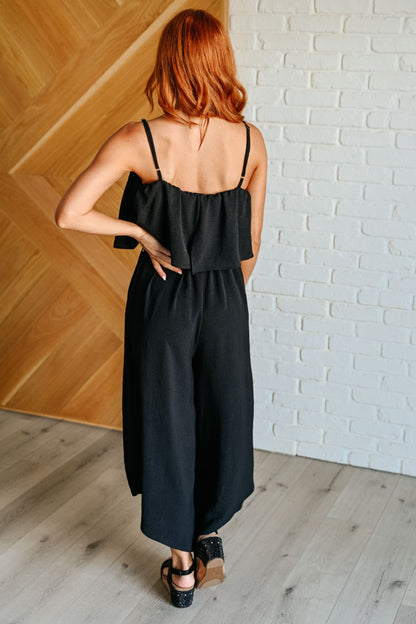 Woman wearing a black dress standing against a white brick wall.