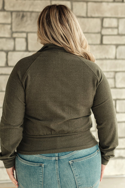 Person wearing an olive green jacket and blue jeans against a stone wall.