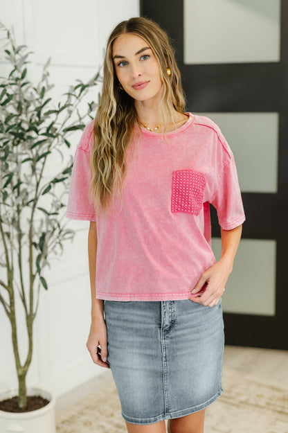 Woman wearing a pink t-shirt with a pocket and denim skirt indoors.