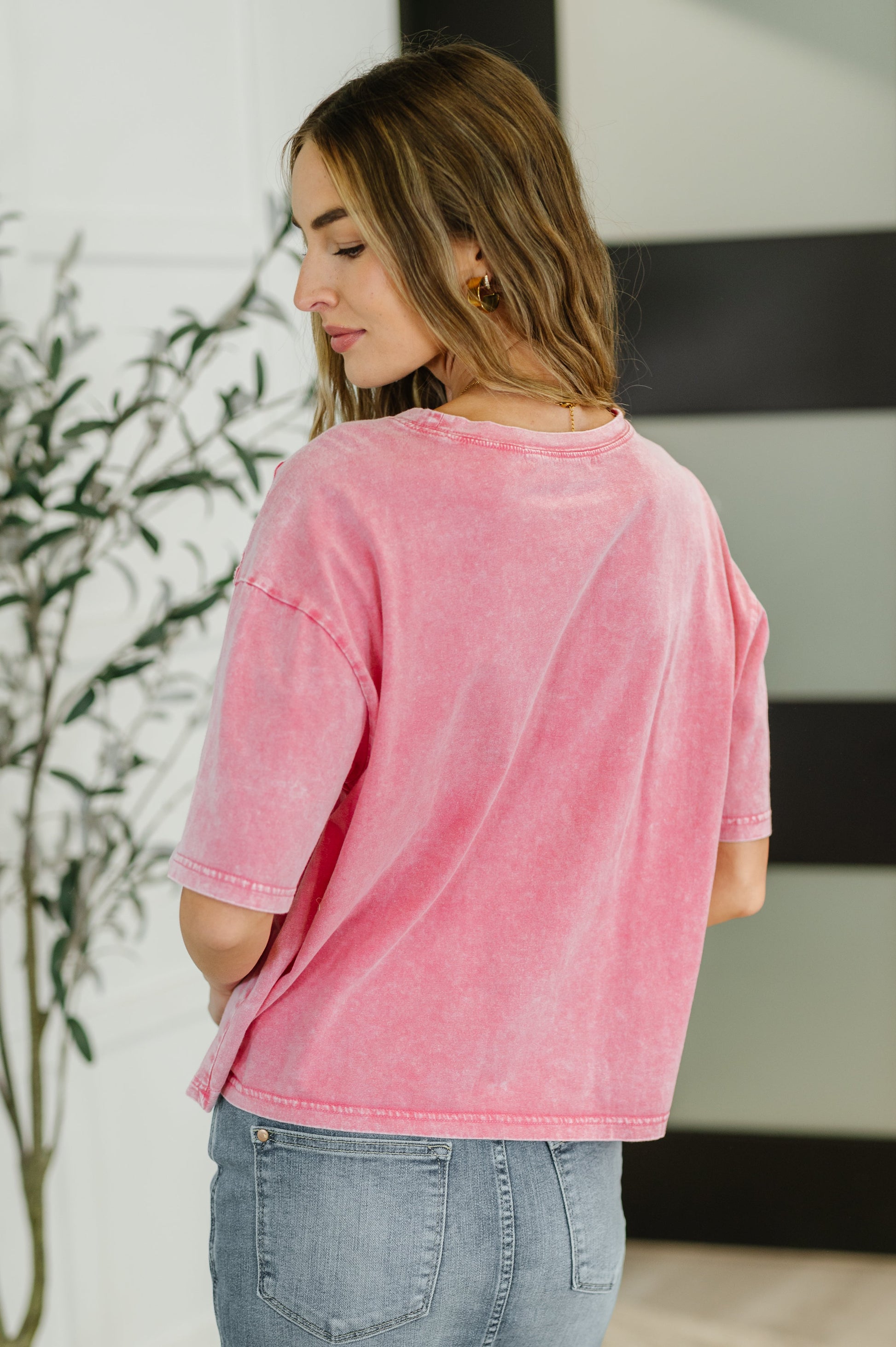 Woman wearing a pink oversized shirt and blue jeans indoors.