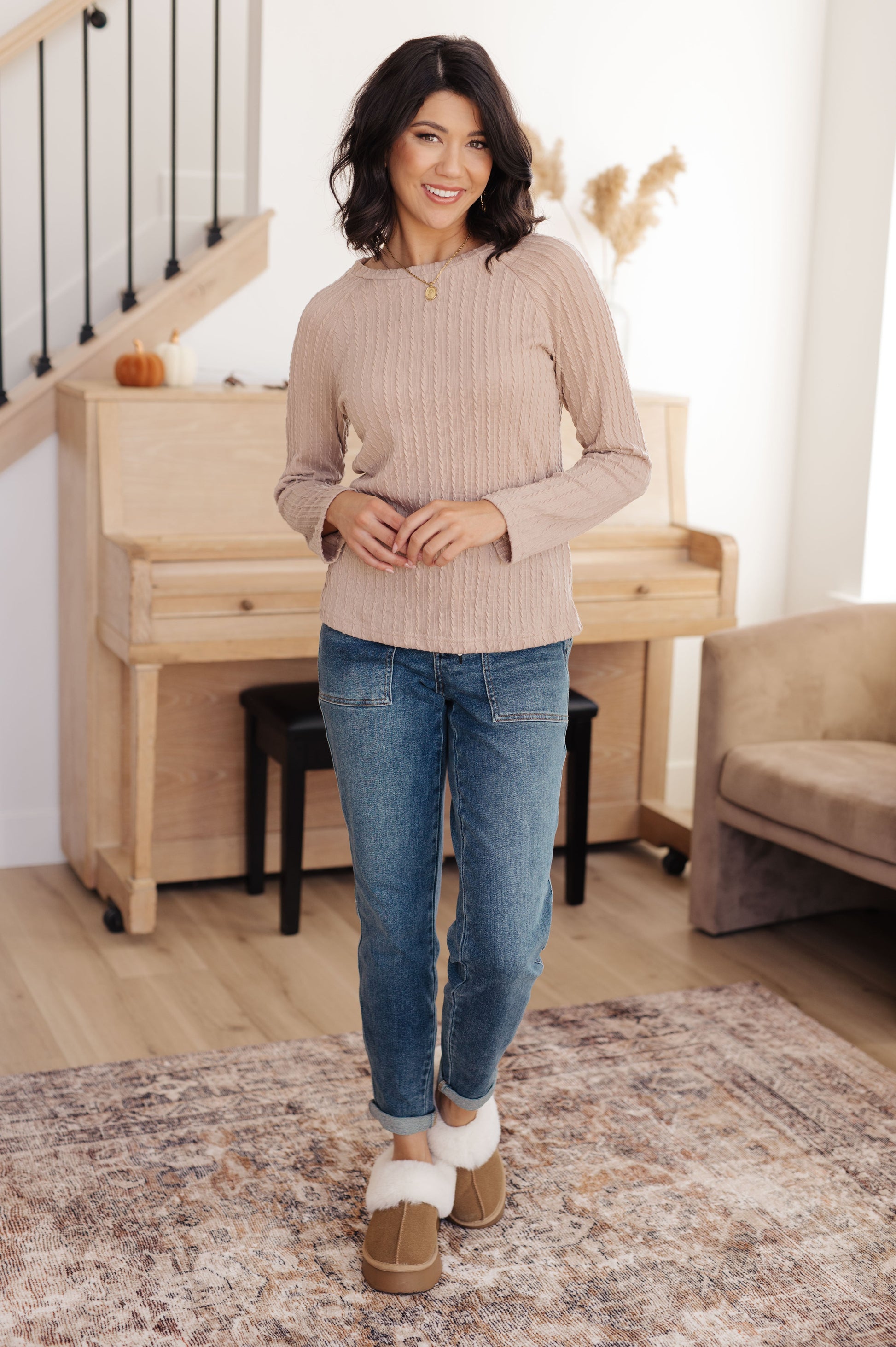 Woman wearing a beige sweater and blue jeans standing in a living room.