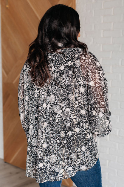 Person wearing a black and white floral patterned kimono against a wooden and white brick wall.