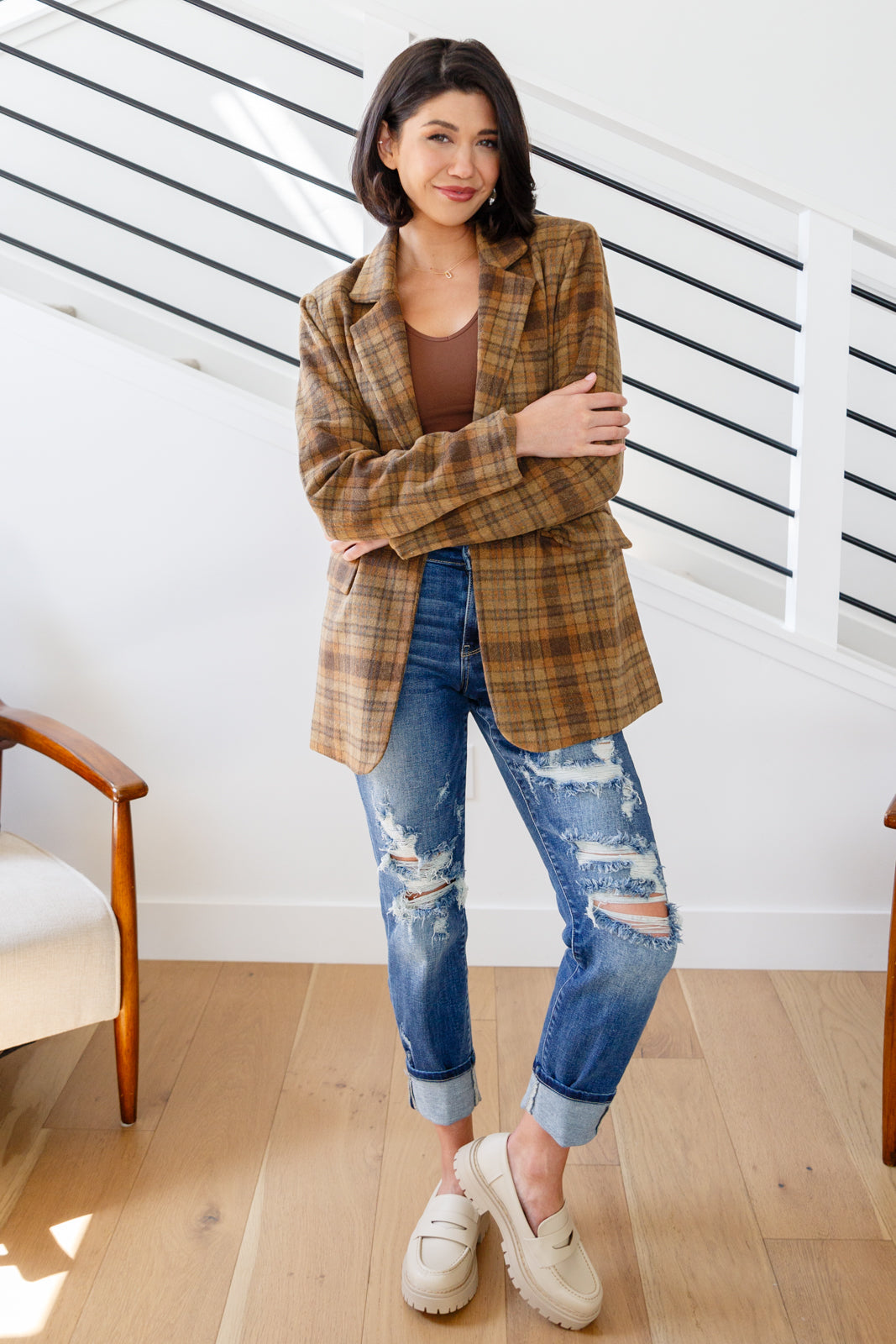 Woman wearing a plaid blazer, brown top, and ripped jeans indoors.