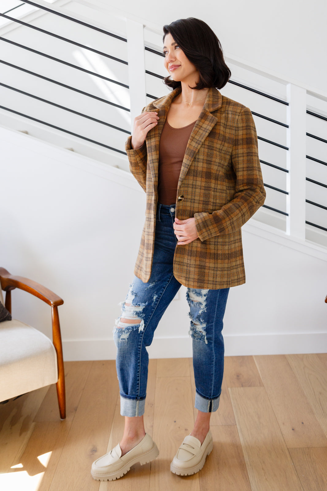 Woman wearing a plaid jacket, brown top, and blue jeans indoors.