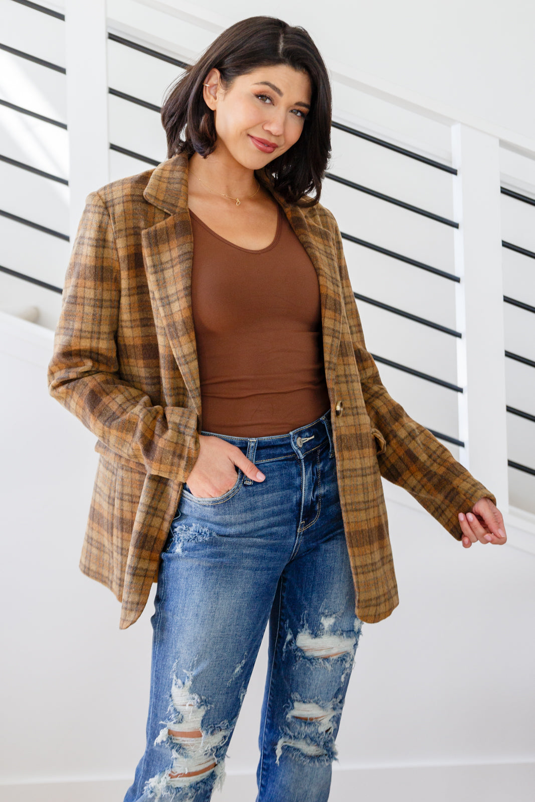 Woman wearing a plaid jacket, brown top, and blue jeans against a white background